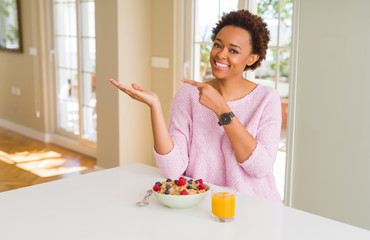 Young african american woman having healthy breakfast in the morning at home amazed and smiling to the camera while presenting with hand and pointing with finger.