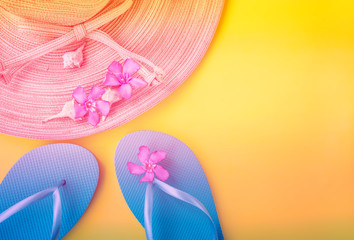 Women's straw hat pink tropical flowers blue slippers sea shells on gradient duotone peachy yellow background. Beach vacation fashion concept