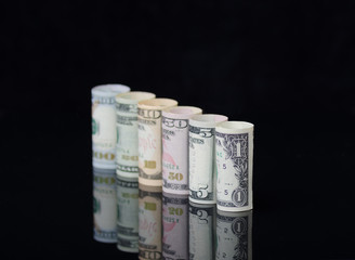 US dollars banknotes rolls on black background with reflection.