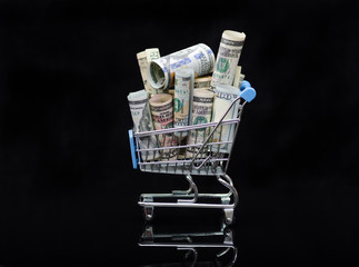 US dollars rolls and shopping cart full packs of bills on black background with reflection.