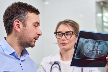 Caucasian female dentist explaining to male patient the x-ray