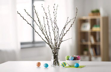 holidays and object concept - pussy willow branches and colored easter eggs in vase on table