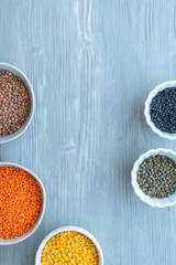 Schüsseln mit verschiedenen Sorten Linsen auf einem hellen Holzhintergrund