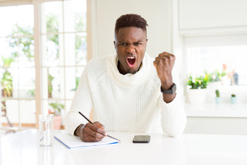 African american student man writing on a paper using a pencil annoyed and frustrated shouting with anger, crazy and yelling with raised hand, anger concept