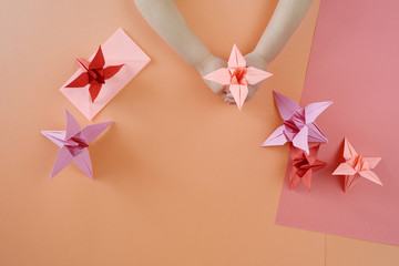 Children's hands do origami from colored paper on living coral background.