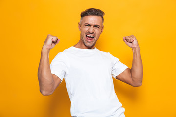 Happy excited man posing isolated over yellow wall background make winner gesture.