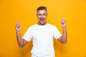 Happy excited man posing isolated over yellow wall background pointing.