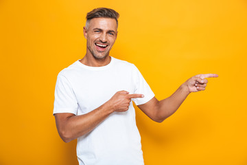 Happy excited man posing isolated over yellow wall background pointing.