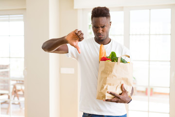 African american man holding paper bag full of fresh groceries with angry face, negative sign showing dislike with thumbs down, rejection concept