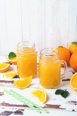 Orange juice in glass jars and fresh oranges on a white wooden rustic background.