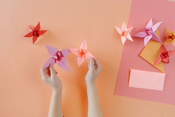 Plakat Children's hands do origami from colored paper on living coral background.