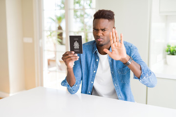 African american man holding passport of Canada with open hand doing stop sign with serious and confident expression, defense gesture