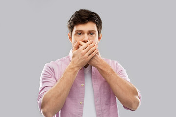 emotion, expression and people concept - shocked and speechless young man covering his mouth by...