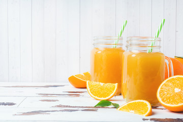 Orange juice in glass jars and fresh oranges on a white wooden rustic background.