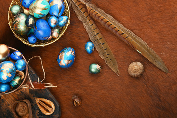 Painted colored Easter eggs in golden bowl and copper mug on red animal skin. Boho stile.