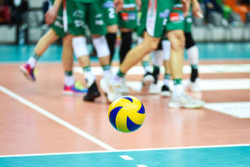 Volleyball ball flying near the pitch with players in the background.