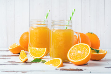 Orange juice in glass jars and fresh oranges on a white wooden rustic background.