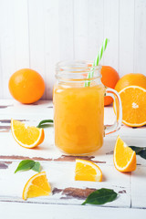 Orange juice in glass jars and fresh oranges on a white wooden rustic background.