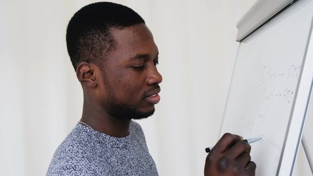 Medium closeup young male African analytic economic worker drawing graphic margin or profit of company on flip chart. Side view creative man making presentation for informal corporate business meeting