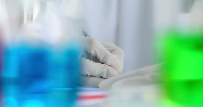 Blurred foreground video scene of scientist hand that recording experiment results, concept for scientist recording experiment results in laboratory room.