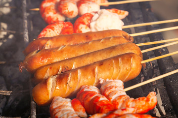 Sausages and shrimps on wooden skewers, baked on the grill, lie on the table with a traditional Asian street food - satay. Close-up