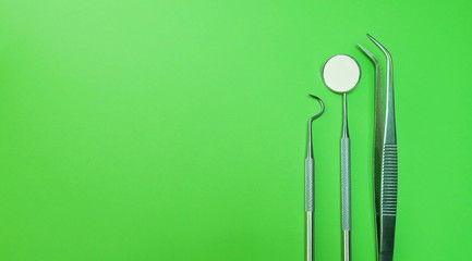 Dentist mirror, forceps curved, explorer curved, dental explorer angular and explorer curved with chip, right at green background. Professional dentist tools in dental clinic or hospital