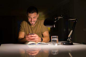Young handsome man studying at home , using smartphone, looking at the phone smiling