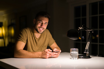 Young handsome man studying at home , using smartphone, smiling at the camera
