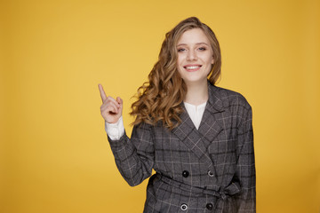 Pretty woman with great smile pointing something isolated over the yellow background