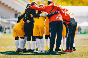 Coach coaching Girls Sports Team. Girls school sports team huddling with coach on the grass field. Soccer football junior girls team at sports outdoor field before match. Coach Building Confidence - Powered by Adobe