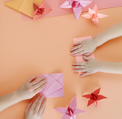 Children's hands do origami from colored paper on living coral background.