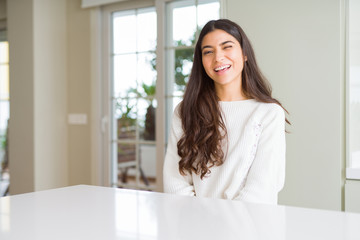 Young beautiful woman at home on white table winking looking at the camera with sexy expression,...