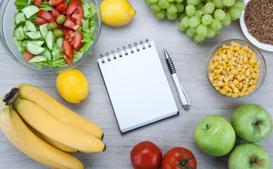 notebook with a diet plan with fresh vegetables and fruits on the table