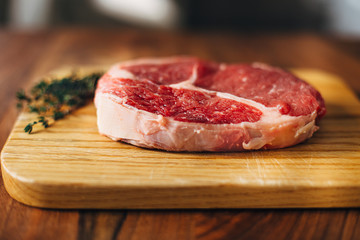 Overhead shot of ribeye steak resting on a wooden board in the kitchen with fresh thyme. Top shot