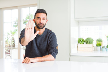 Fototapeta premium Handsome hispanic man wearing casual sweater at home doing stop sing with palm of the hand. Warning expression with negative and serious gesture on the face.