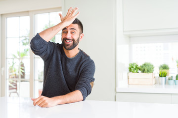 Handsome hispanic man wearing casual sweater at home surprised with hand on head for mistake,...