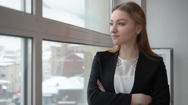 Serious businesswoman in black suit looking to window in modern office. Impatient woman standing near window in business office. Business people concept