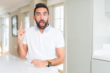 Fototapeta premium Handsome hispanic man casual white t-shirt at home pointing finger up with successful idea. Exited and happy. Number one.