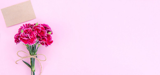 May mothers day idea concept photography - Beautiful blooming carnations tied by bow with kraft text card isolated on bright modern table, copy space, flat lay, top view, mock up