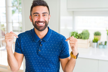 Handsome hispanic man at home looking confident with smile on face, pointing oneself with fingers...