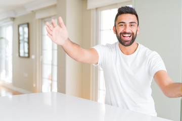 Fototapeta na wymiar Handsome hispanic man casual white t-shirt at home looking at the camera smiling with open arms for hug. Cheerful expression embracing happiness.
