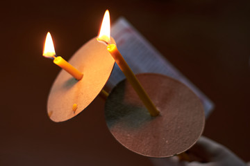 Two church candles and a sheet of prayer in the hand on a dark background