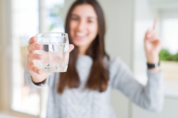 Beautiful young woman drinking a fresh glass of water very happy pointing with hand and finger to the side