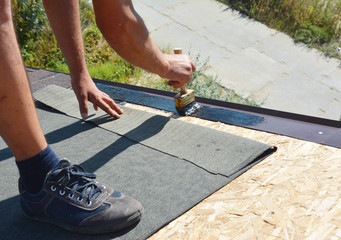 Roofer contractor gluing waterproof membrane on wooden roof top surface with brush and black bitumen  spray on tar before installing asphalt shingles. © bildlove