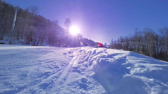 SLOW MOTION: Young pro snowboarder riding the half pipe in big mountain snow park, spraying snow into camera on halfpipe wall in sunny winter. Extreme snowboarder snowboarding and doing tricks.