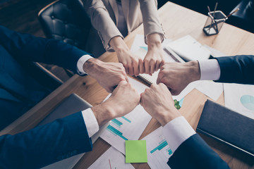 Cropped top above high angle view of three elegant stylish sales managers putting fists together in round circle over table desk documents in loft industrial interior work place station