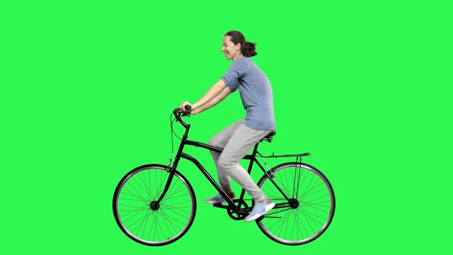A Young woman riding a bicycle over a green screen,  looking around., waving hello. No motion blur for optimal keying.