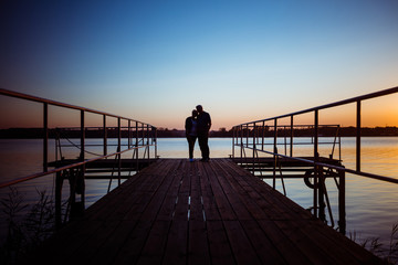 Silhouette couple embracing on pier during sunset