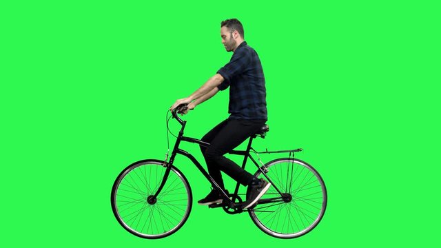 Cute man riding a bicycle over green screen, looking around and upwards, waving hello. No motion blur for optimal keying.