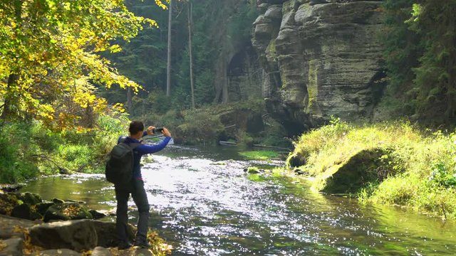 Female tourist with backpack taking pictures of the autumn scenery by smartphone 